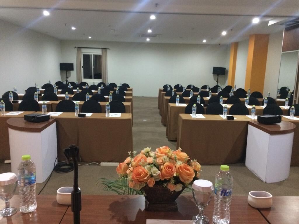 Un salón de conferencias con filas de mesas, cada una con un micrófono, una botella de agua y un bloc de notas.