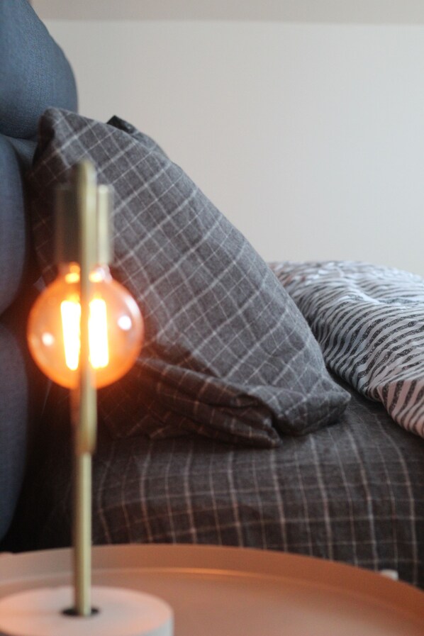 A lamp with a spherical shade on a white base, placed on a surface with a checkered pillow in the background.