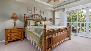 A bedroom with a wooden bed, two bedside tables with lamps, a ceiling fan, and a large window with a view of trees.