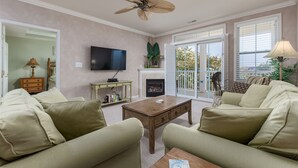 A living room with a fireplace, a television, and a ceiling fan.
