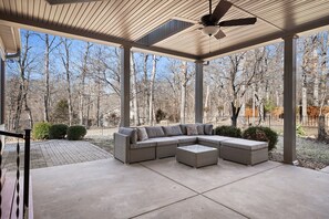 A covered patio with a sectional sofa, a ceiling fan, and a view of a wooded area. - Luxe Innsbrook Resort Home - Lakes/Golf/Trails (Wright City)