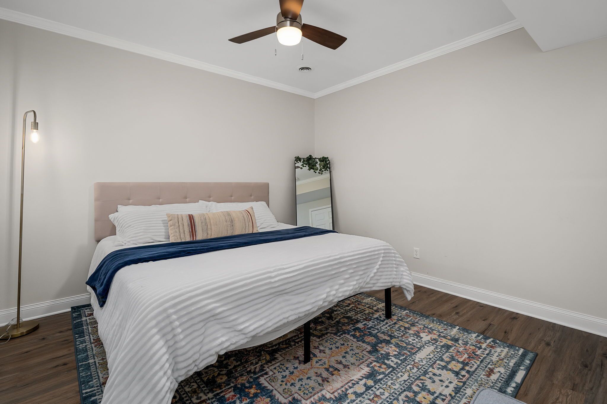 Une chambre à coucher avec un lit, un ventilateur de plafond, une lampe sur pied et un tapis à motifs.