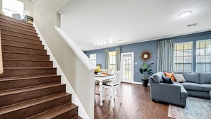 A modern living room with a staircase, a gray sofa, and a dining area.