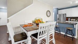 A dining area with a wooden table, white chairs, and a fruit basket.