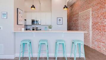 A modern kitchen with white cabinets, a brick wall, and three light blue bar stools.