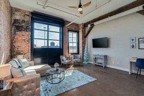A spacious living room with a large window, a sofa, a coffee table, and a TV mounted on the wall.