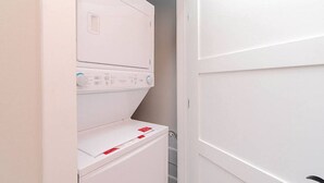 Uma lavanderia com máquinas de lavar e secar empilhadas, um escorredor de metal e uma porta branca.