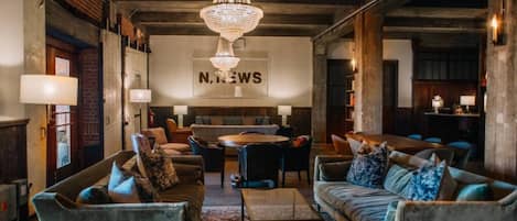 A spacious lounge area with a large chandelier, comfortable seating, and a prominent 'N. NEWS' sign on the wall.