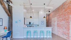 Cozinha moderna com ilha central, banquetas e parede de tijolos.