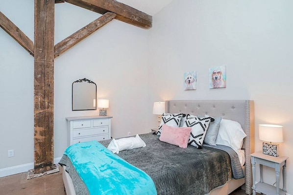 Une chambre à coucher comprenant un lit, des tables de chevet, une commode, un miroir et des œuvres d’art murales.