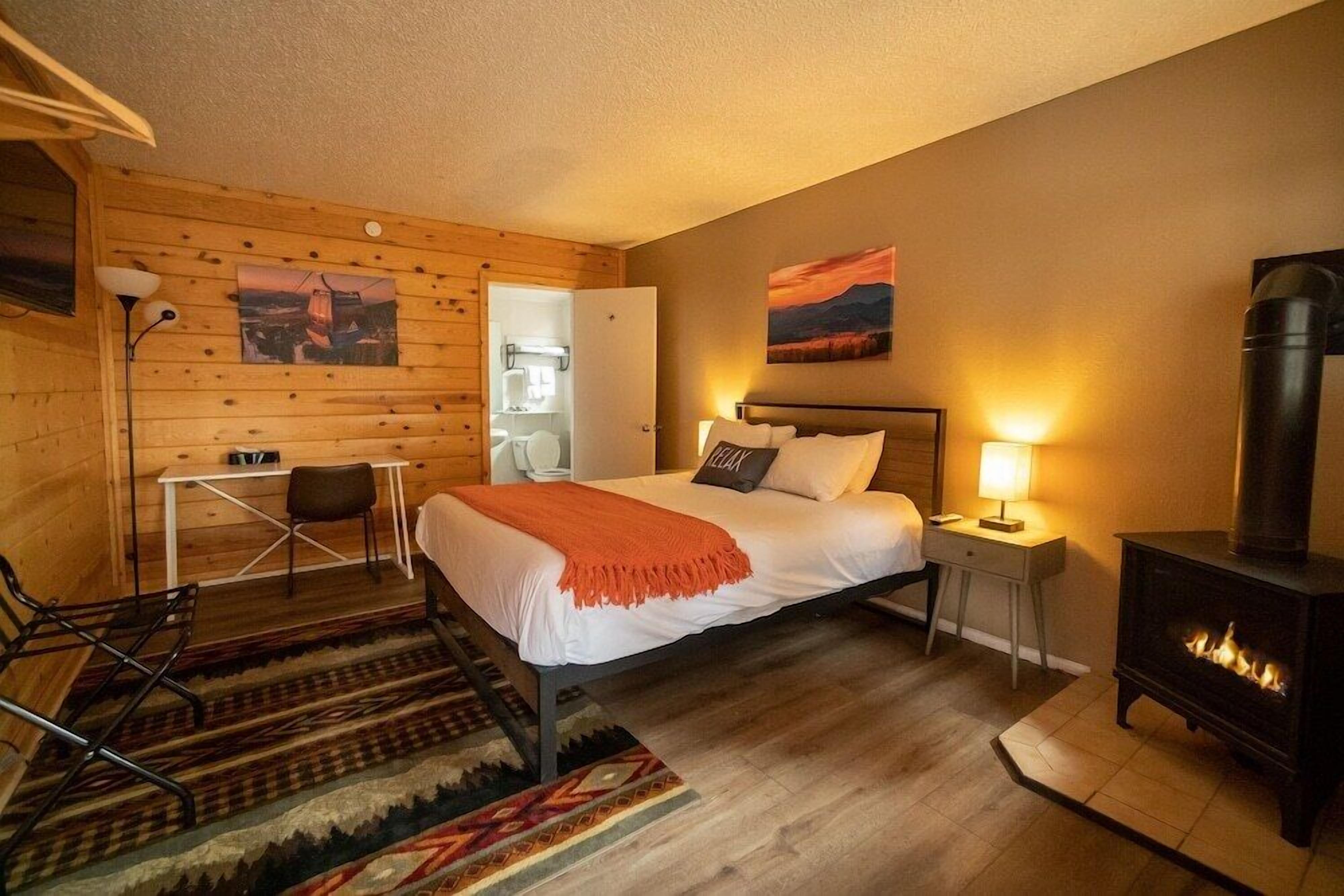 A cozy room with a bed, a desk, a chair, a fireplace, and wooden walls.