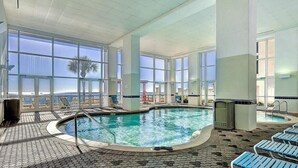 Una piscina interior con paredes de vidrio transparente, sillones de descanso y suelo de baldosas.