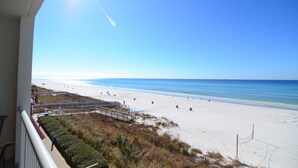Una playa con cielo despejado, orilla de arena y algunas personas caminando.