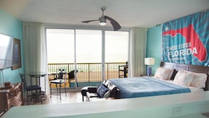 Habitación de hotel con cama, escritorio, silla y balcón con vistas a la playa.