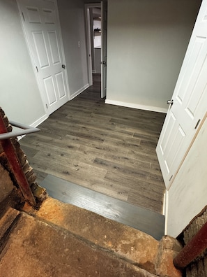 A hallway with wooden flooring, white doors, and a staircase with a red handrail.
