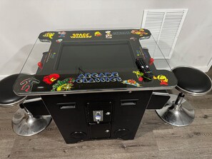 A gaming table with arcade classic characters, a remote control, and two chairs. - Carrollton Square's exclusive VRBO Suite. (Carrollton)