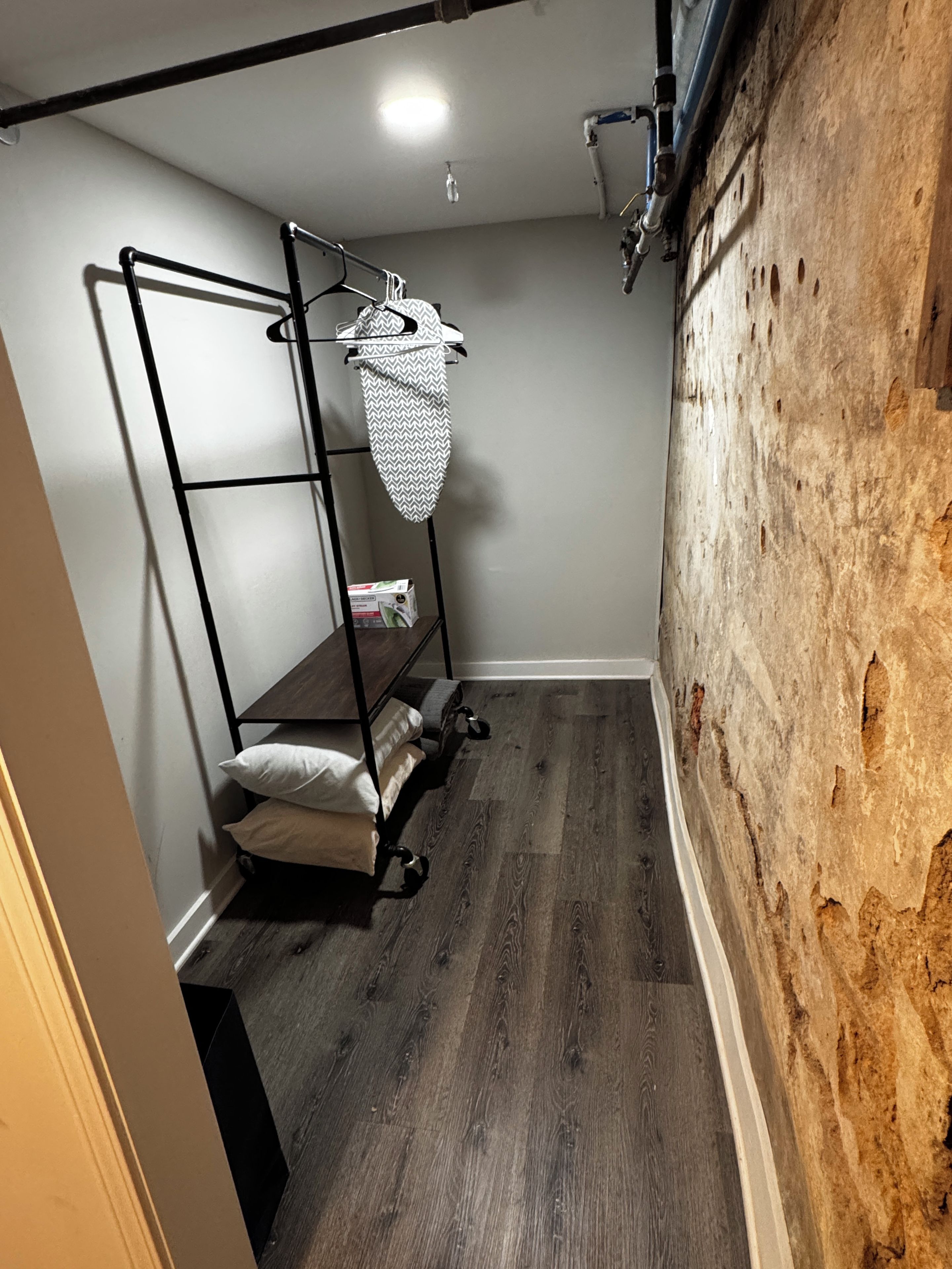 Una habitación de esquina con una estantería metálica, un bolso colgado y suelo de madera.