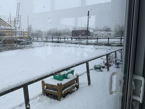 A snowy outdoor area with a metal fence, a wooden bench, and some green crates.