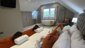 A hotel room with a large bed, a sofa, a bathtub, and a window with curtains. - Pendle View Sleeps 8 with Hot Tub (Longridge, Preston)