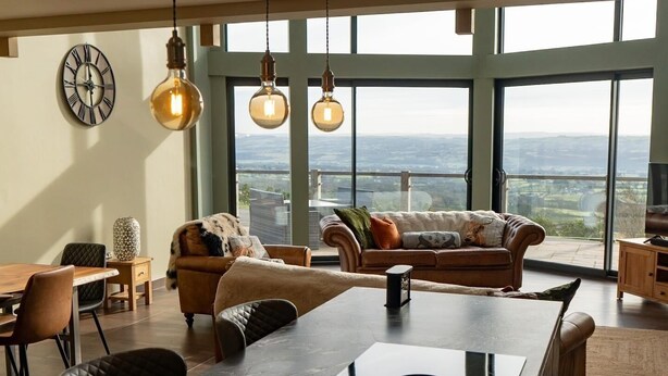 A spacious living area with a large dining table, two sofas, and a view of the city through large windows. - Pendle View Sleeps 8 with Hot Tub (Longridge, Preston)