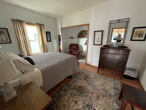 Ein Schlafzimmer mit einem Bett, einem Schminktisch, einem Sessel und einem großen Spiegel.