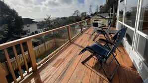 Une terrasse en bois dotée d’une balustrade en verre, de mobilier d’extérieur et offrant une vue sur les maisons et les arbres.