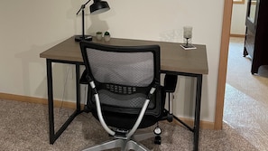 Un espace de travail comprenant un bureau, une chaise, une lampe et un verre de vin.