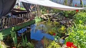Ein Garten mit Teich, Holzzaun und roten Blüten.