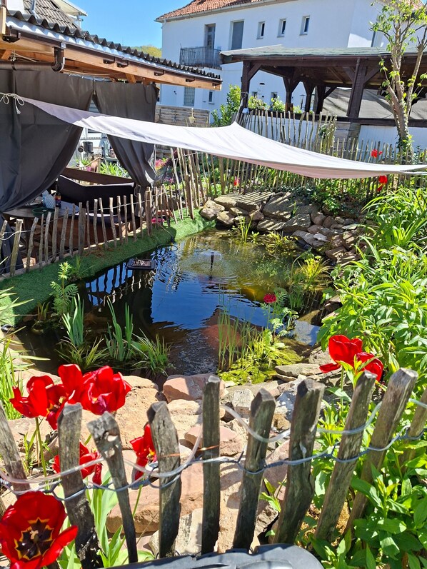 Un jardin avec un étang, une clôture en bois et des fleurs rouges.