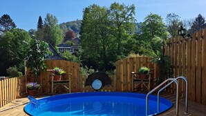 Eine Holzterrasse mit einem blauen Pool, umgeben von Holzzäunen und Topfpflanzen.