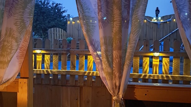 Eine Holzterrasse mit Geländer, einem Holzzaun und Lichterketten.