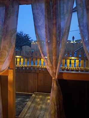 Une terrasse en bois avec une rambarde, une clôture en bois et des guirlandes lumineuses.