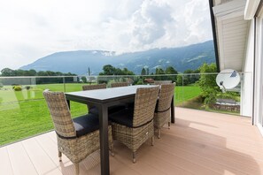 A balcony with a table and chairs, a glass railing, and a view of mountains.