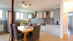 Een moderne keuken met witte kastjes, een zwart-wit betegelde achterwand en een eethoek met een houten tafel en stoelen.