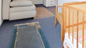 Een kamer met een schuine kap, een bank, een babybedje, een klein tafeltje en een kamerkleed met een patroon.