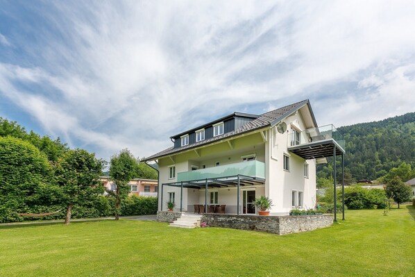 A two-story house with a balcony, a stone foundation, and a grassy yard.