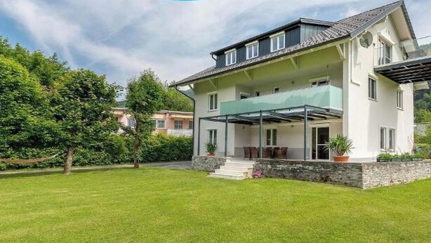 A two-story house with a covered patio, stone foundation, and a view of a forested hill. - Apartment 'Villa Müller Rotfuchs' with Lake View, Shared Garden and Wi-Fi (Ossiach)