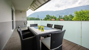 A balcony with a table and chairs, a hanging chair, and a view of mountains and trees. - Apartment 'Villa Müller Rotfuchs' with Lake View, Shared Garden and Wi-Fi (Ossiach)