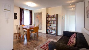 A living room with a sofa, a dining table with chairs, a bookshelf, and a large window. - Apartment 'Villa Müller Rotfuchs' with Lake View, Shared Garden and Wi-Fi (Ossiach)