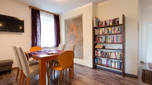 A room with a wooden dining table, four chairs, a bookshelf, and a flat-screen TV mounted on the wall. - Apartment 'Villa Müller Rotfuchs' with Lake View, Shared Garden and Wi-Fi (Ossiach)