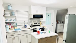A modern kitchen with white cabinets, a stainless steel refrigerator, a microwave, and a wooden island with various kitchen items. - 2 bd 1 bath home - King bed - close to beaches&downtown - backyard with firepit (Pensacola)