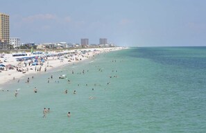 A beach with people swimming and sunbathing, a sandy shore, and buildings in the background.
