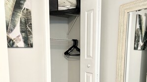 A walk-in closet with a hanging rod, a door, and a mirror with a decorative frame. - 2 bd 1 bath home - King bed - close to beaches&downtown - backyard with firepit (Pensacola)