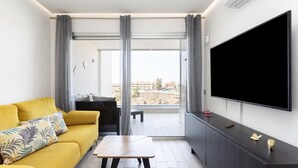 A modern living room with a yellow sofa, a wooden coffee table, a TV, and a balcony with curtains. - Beautiful Vacation Home with Sea Views in the Ocean Garden Complex (Adeje)