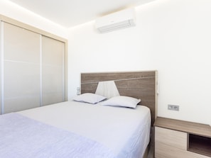 A modern bedroom with a bed, bedside tables, and an air conditioning unit.
