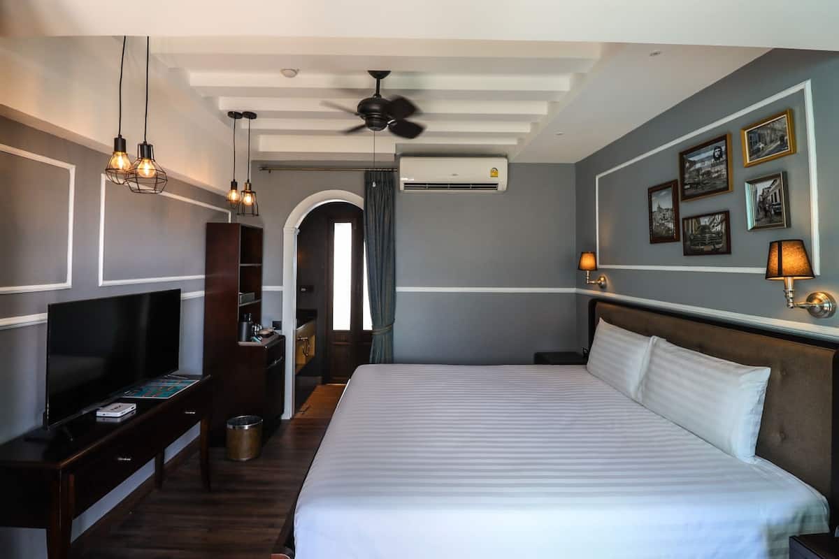 Hotelkamer met een groot bed, een televisie op een standaard, een plafondventilator en een muur met ingelijste foto's.
