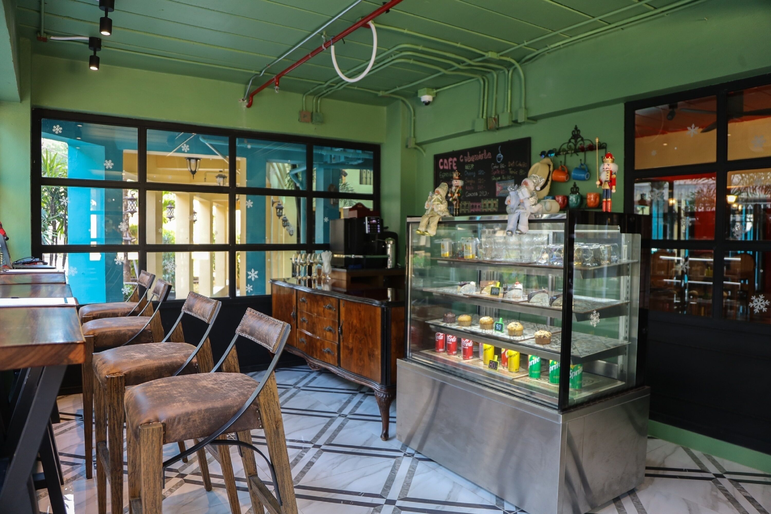 A cafe with wooden chairs, a glass display case with pastries, and a chalkboard menu.