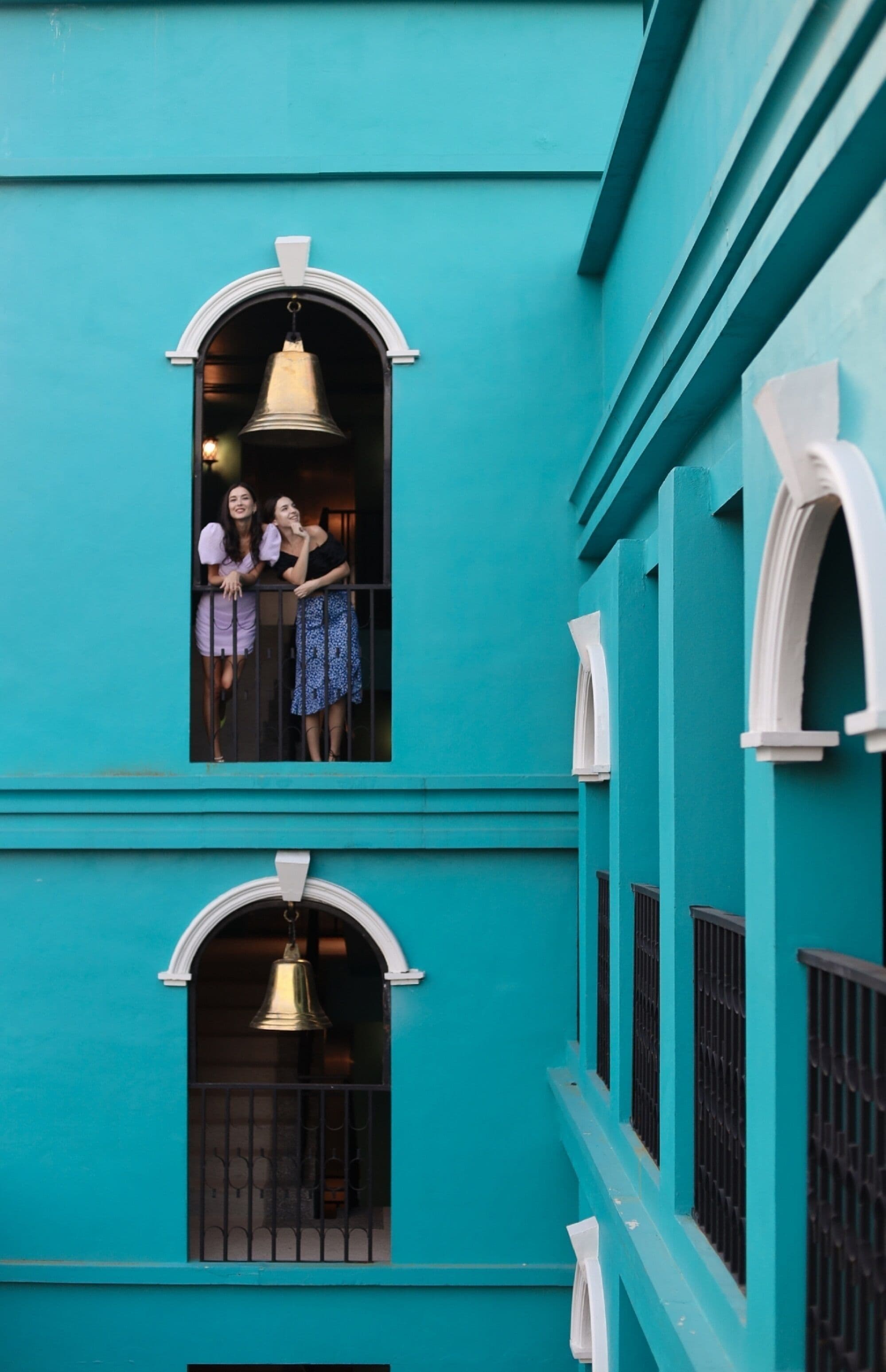 A turquoise building with two arched windows, each with a bell hanging inside.