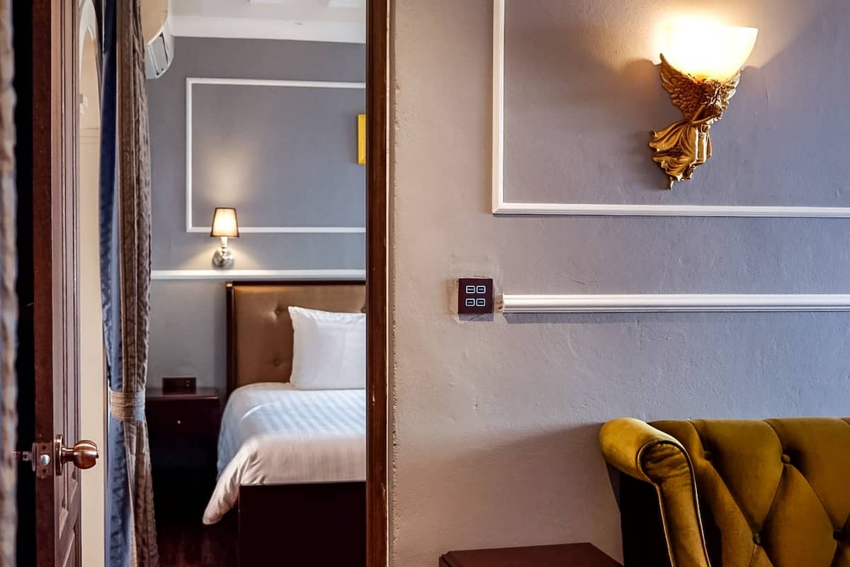 Een hotelkamer met een bed, nachtkastje, lamp, wandlamp en een deur.