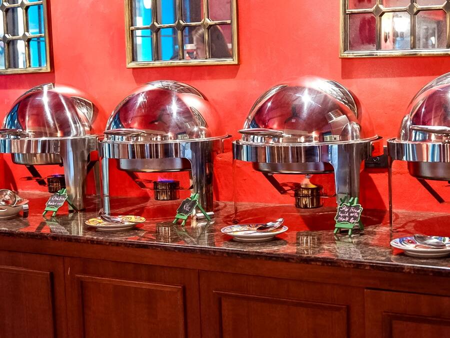 A buffet setup with multiple food service stations, each with a dome cover and a small sign indicating the type of food served.